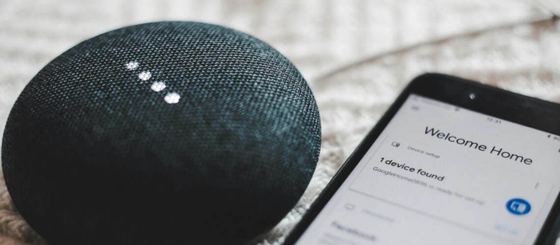 turned-on charcoal Google Home Mini and smartphone