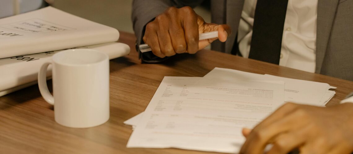 Free Close-up of a businessman holding and reviewing documents on a wooden desk. Stock Photo